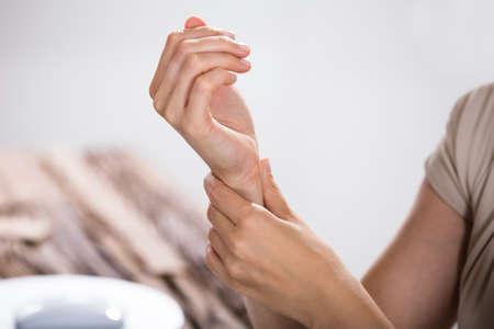 Close-up Of A Businessperson Holding Painful Wrist Over Wooden Deskの写真素材