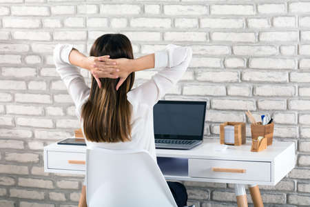 Rear View Of A Young Businesswoman Sitting On Chair Stretching Her Armsの写真素材
