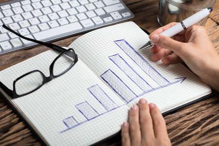 Close-up Of A Businessperson's Hand Drawing Graph With Pen On Notebookの写真素材