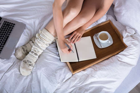 Elevated View Of Woman Writing In Diary With Cup Of Coffee On Trayの写真素材