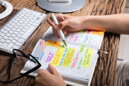 High Angle View Of A Businessperson Writing Schedule In Diary Over Wooden Deskの写真素材