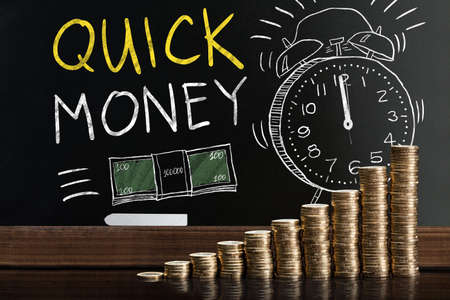 Quick Money Words On Blackboard Behind Stacked Coinsの写真素材