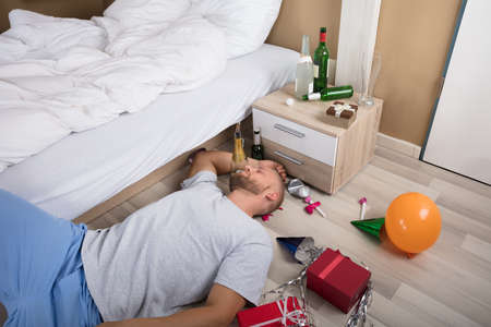 Man Sleeping On Messed Up Hardwood Floor With Beer Bottles On Nightstand