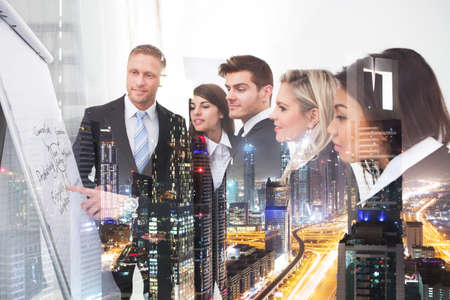 Multiethnic business people planning together over illuminated cityscape backgroundの写真素材