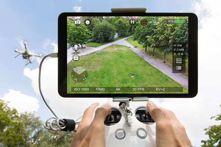 Cropped image of hands controlling drone filming park seen on digital tablet