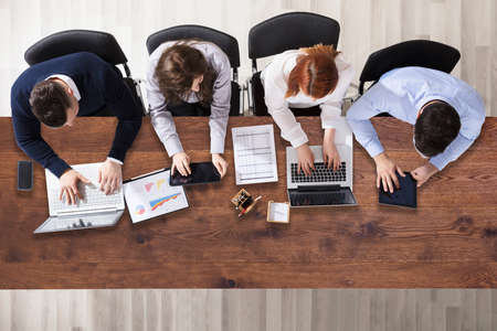 High Angle View Of Businesspeople Working In Office Over Wooden Deskの写真素材