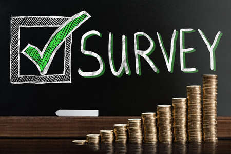 Customer Satisfaction Survey On Blackboard Behind Stacked Coinsの写真素材