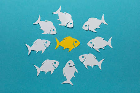 Yellow Fish Surrounded By White Paper Fishes Over Blue Backgroundの写真素材