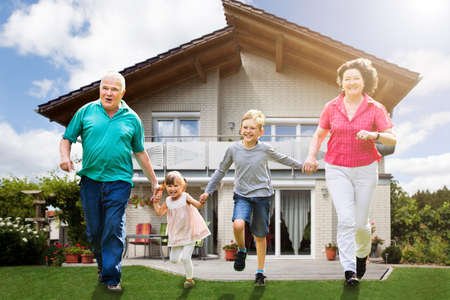 Smiling Grandparents Running With Their Grandchildren In Front Of Their Houseの写真素材