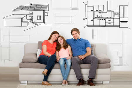 Happy Family Sitting On Couch Against House Blueprint In Living Roomの写真素材