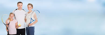 Happy Family Holding Rackets And Ball Against Blue Sky