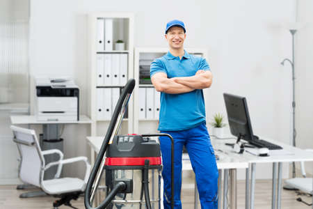Portrait Of A Smiling Young Male Cleaner With Arms Crossed Standing In Officeの写真素材