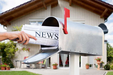 Close-up Of Hand Taking Newspaper From Mailbox In Front Of Their Houseの写真素材