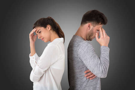 Young Frustrated Couple Standing Back To Back On Gray Backgroundの写真素材