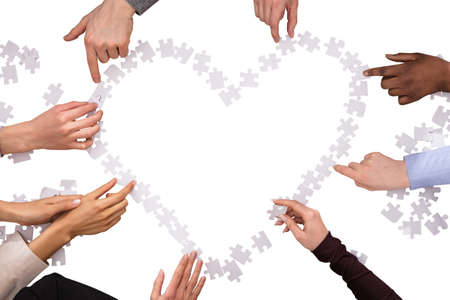 Group Of Hands Making Heart Shape With Jigsaw Puzzles Over White Background