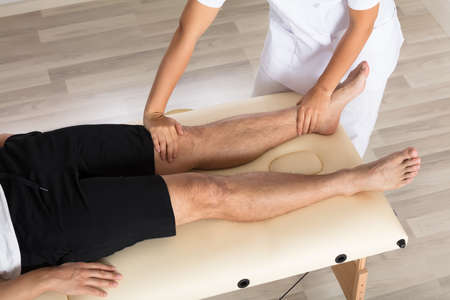 Young Female Physiotherapist Massaging Man's Leg In Clinicの写真素材