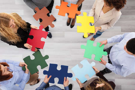 Elevated View Of Business People Holding Colorful Jigsaw Puzzles In Office