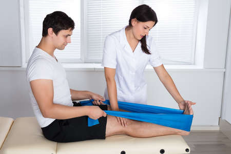 Female Therapist Assisting Male Patient While Stretching His Leg In Hospital