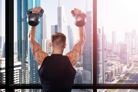 A Muscular Man Training With Kettles Overlooking The City Skyline From The Gym Windowの写真素材