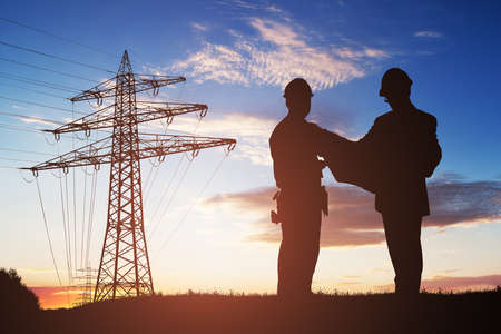 Silhouette Of Two Engineers Discussing Together With Electricity Pylon In Backgroundの写真素材