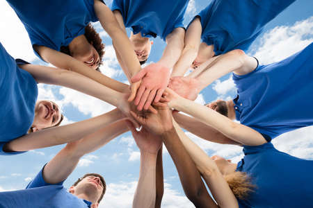 Happy Multiracial Janitors Stacking Hands Against Cloudy Sky