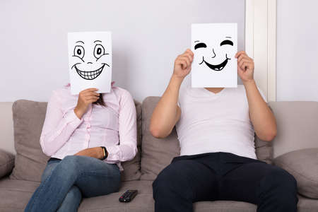 Couple Holding Smiling Faces In Front Of Their Faces Sitting On Couchの写真素材