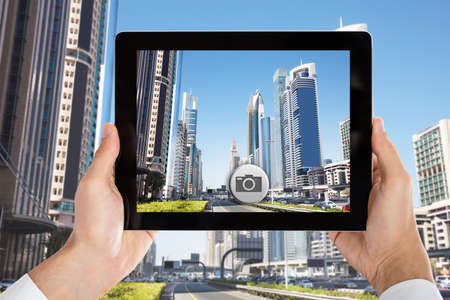 Close-up Of Person's Hand Holding Tablet Taking Pictures Of City Skyscrapers In Dubaiの写真素材