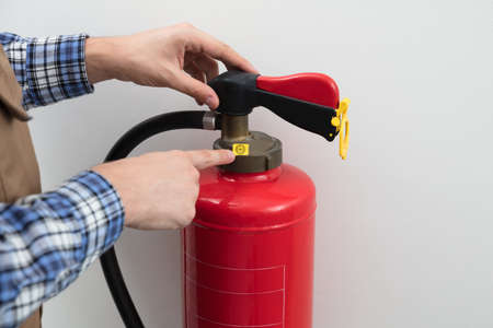 Close-up Of Technician's Hand Pointing To Symbol On Red Fire Extinguisher Against White Backgroundの写真素材