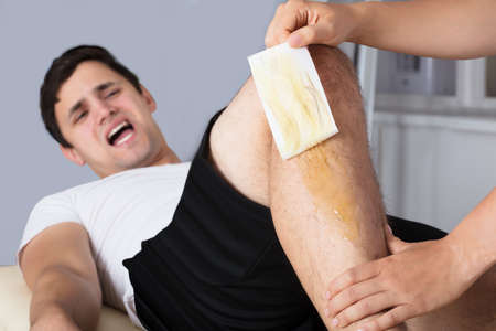 Man Screaming In Pain While Waxing Leg With Wax Stripの写真素材