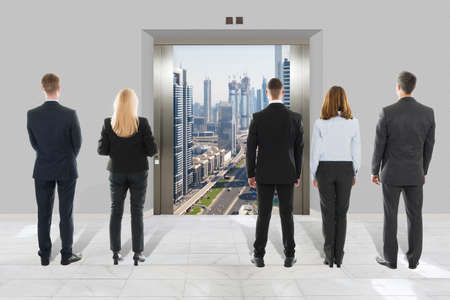 Rear View Of Businessman And Businesswoman Looking At Modern Elevator With Opened Door To City