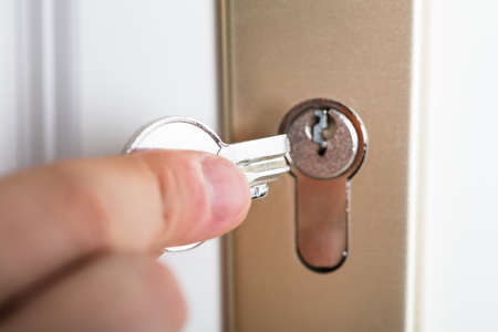 Close-up Of Person's Hand Holding Broken Key Inserting In Keyholeの写真素材
