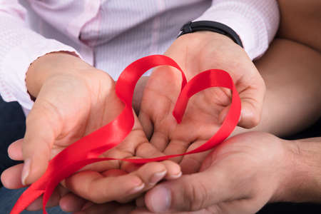 Close-up Of Couple's Hand Holding Heart Shape Red Ribbonの写真素材