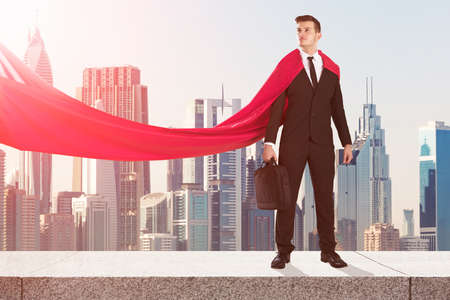 Young Superhero Businessman Standing On Surrounding Wall With City Skyscrapers Buildings In Backgroundの写真素材