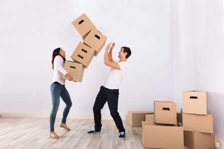Young Woman Falling Stack Of Cardboard Boxes Over The Man In Houseの写真素材