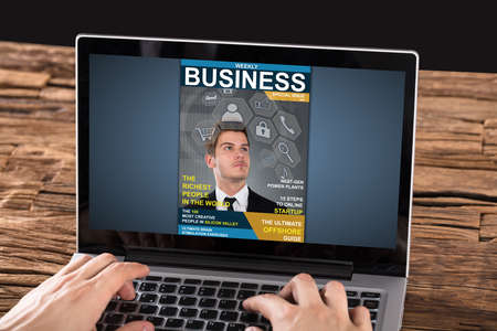 Close-up Of Person Looking At Magazine On Laptop At Deskの写真素材