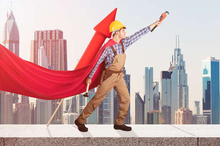 Superhero Handyman With Worktools And Red Rocket Standing On Wall Against City Buildingsの写真素材
