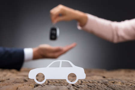 Close-up Of Car Dealer Giving Key To Businessperson With White Car On Wooden Deskの写真素材