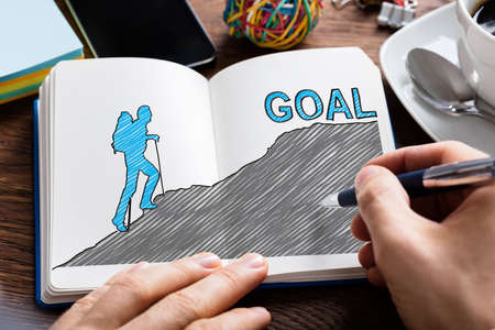 Person's Hand Drawing Goal Concept On Notebook In Office