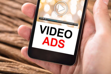 Close-up Of Person's Hand Holding Mobile Phone With Text Video Ads On Screen
