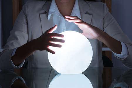 Close-up Of Businesswoman Hand On Crystal Ball On Table In Office