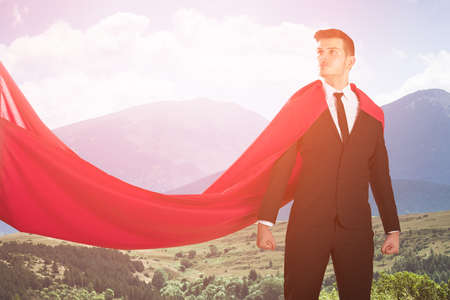Young Confident Super Businessman In Red Cape Against Scenic Backgroundの写真素材