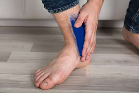 Close-up Of Person's Hand Holding Ice Gel Pack On Ankle At Homeの写真素材