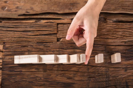 High Angle View Of Person's Hand Stopping Dominoes Continue Toppled At Wooden Deskの写真素材