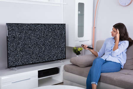 Rear View Of A Woman On Sofa Getting Frustrated With Glitch TV Screen At Home