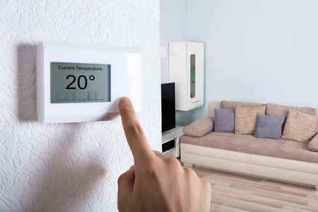 Close-up Of A Person's Hand Adjusting Digital Thermostat At Home