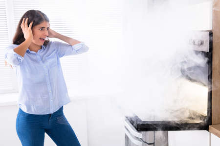 Shocked Young Woman Looking At Smoke Coming From Oven In Kitchenの写真素材