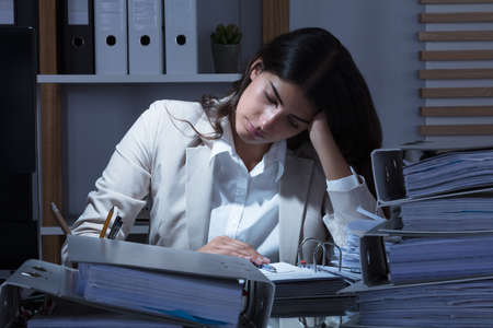 Stressed Young Businesswoman Working At Office With Stack Of Folders On Desk In Officeの写真素材