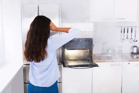 Shocked Young Woman Looking At Smoke Coming From Oven In Kitchenの写真素材