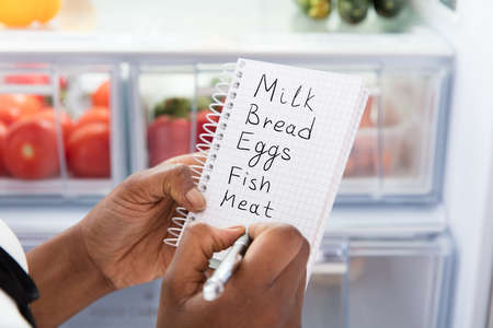 Close-up Of Young African Woman Writing Shopping List Near Open Refrigeratorの写真素材