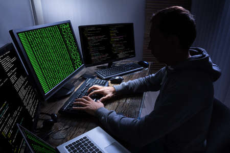 Side View Of Hacker Stealing Information From Multiple Computers On Wooden Deskの写真素材